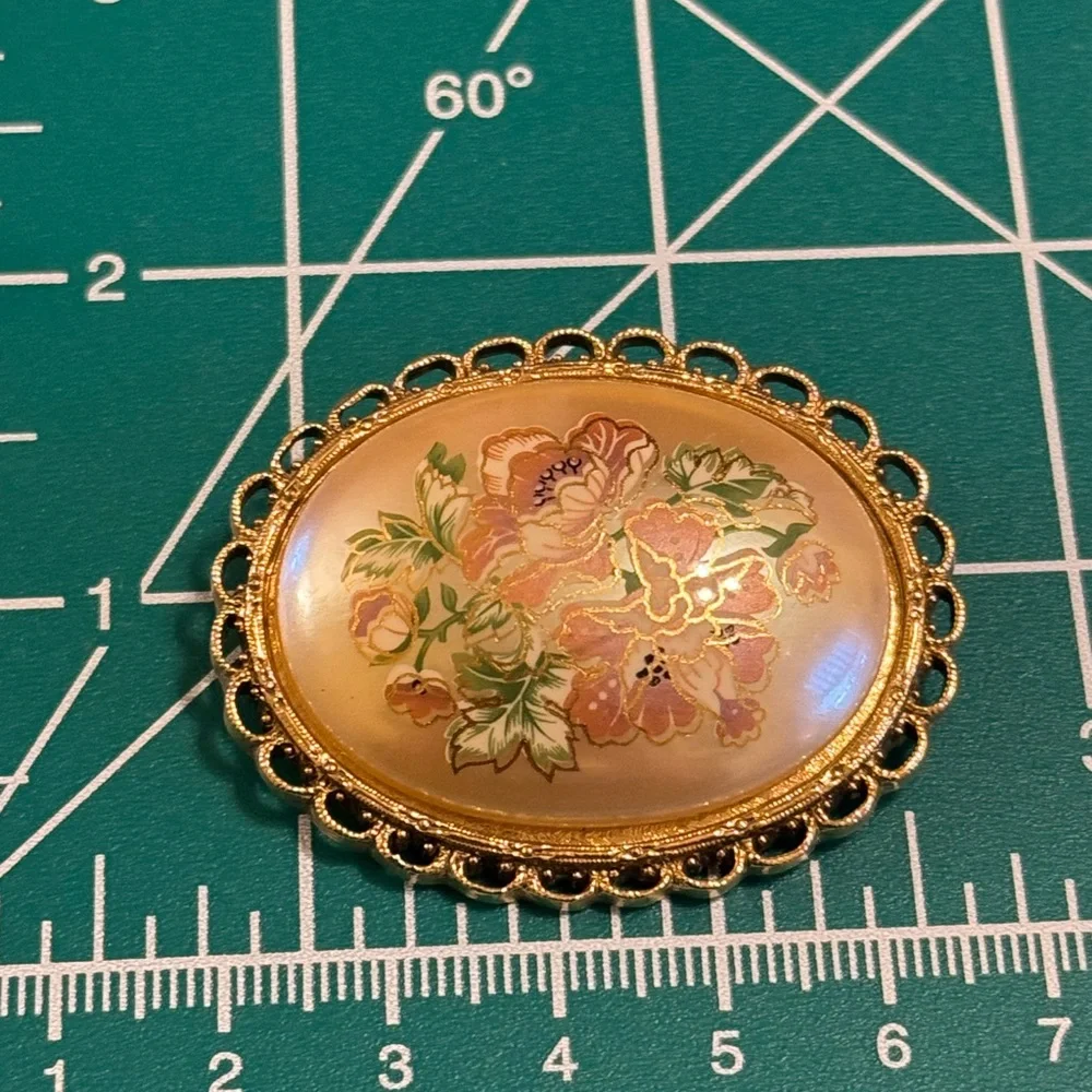 Vintage hand painted floral celluloid set in gold tone filigree frame brooch